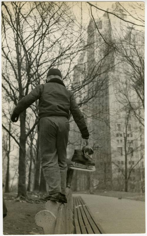 New York City boy standing on park bench while holding ice skates