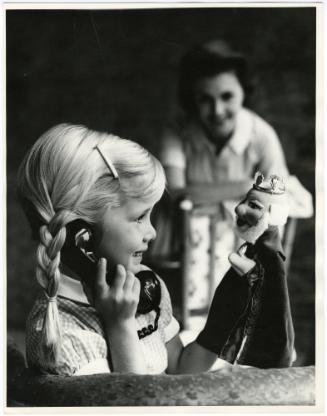 Blonde girl holding telephone and puppet while mother watches