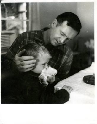 [Father helping young son blow nose into handkerchief]