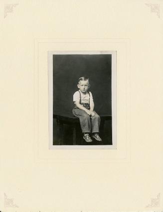 Boy in overalls seated on table