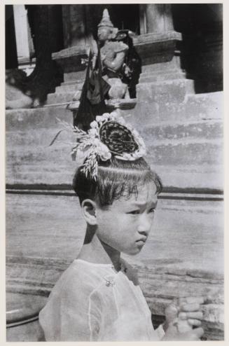 Burmese girls under 8 years of age cut their hair with a fringe which hangs down in a circle around their heads, with a bun and flowers on top. Rangoon,