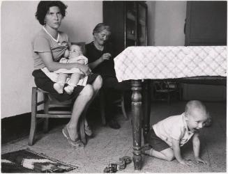 Mother breastfeeding one child while another is under the table, Sicily