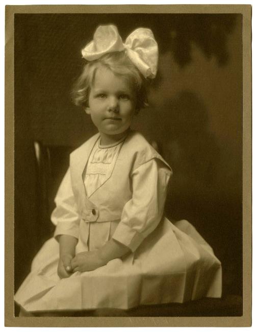 Portrait of seated child, large white bow on top of head