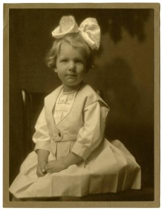 Portrait of seated child, large white bow on top of head