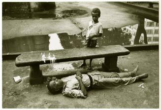 Rio [Man lying on ground in front of bench]