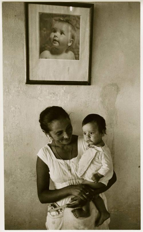 Mother holding an infant under a portrait of an infant, El Salvador