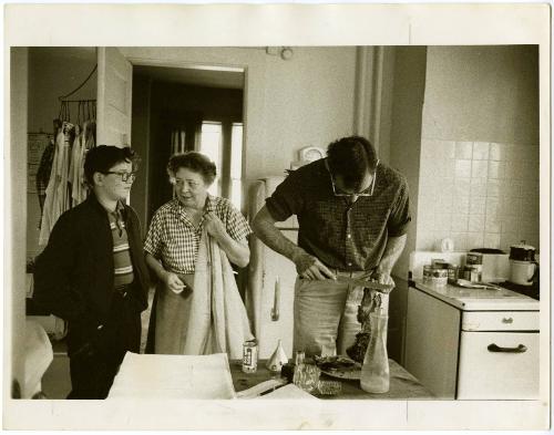 Father carving meat with boy with glasses and grandmother waiting in kitchen, from the series Big Brother