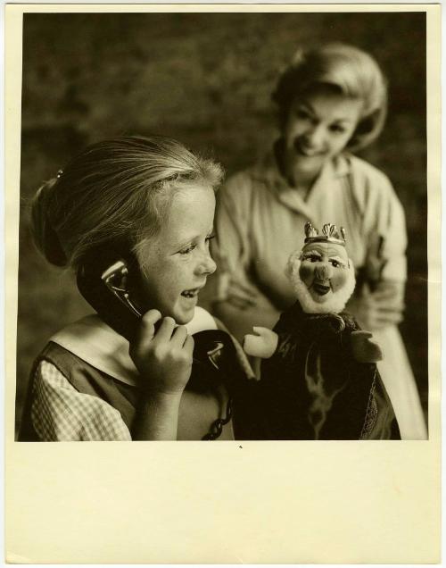 Girl holding telephone and puppet while mother watches