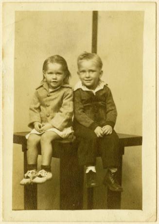 Brother and sister seated on table, striped background