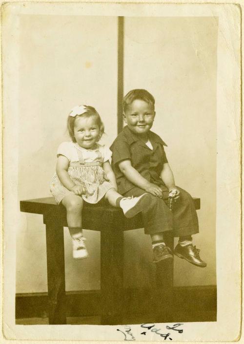 Phyllis and J.C. [Sister and brother seated on table, striped background]