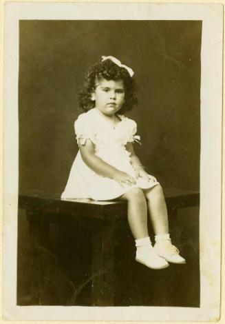 Girl with bow in hair seated on table