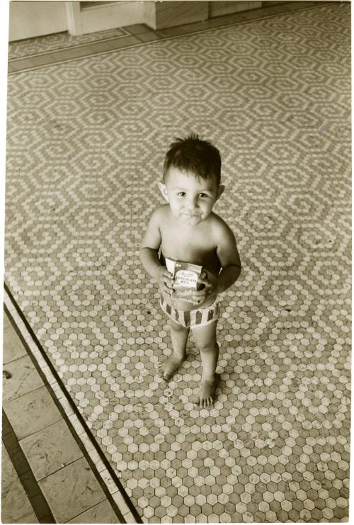 Shirtless boy with chocolate milk in refugee housing after Hurricane Carla, Galveston, Texas