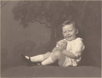 Portrait of seated toddler, in white stockings, smiling, stuffed doll in hand