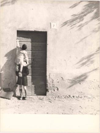 Child lifting another child to ring doorbell, Italy