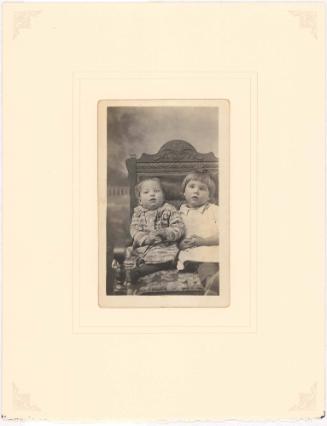 Young brother and sister seated on carved bench, cloud background