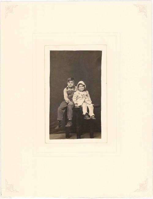 Boy in overalls and girl in winter coat seated on table