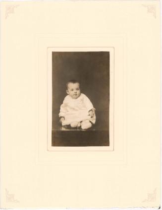 Bemused infant seated on table