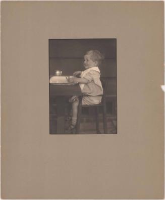 Portrait of smiling toddler (male), seated in high chair at table, eating from bowl