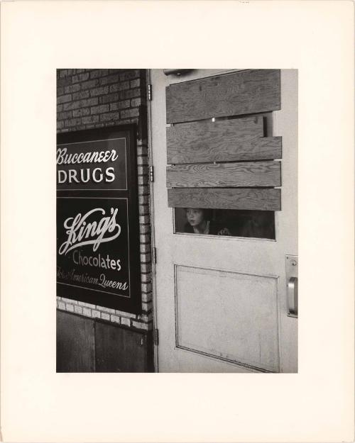 Girl peering through boarded-up door, Galveston, Texas