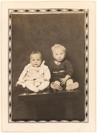 Two infants seated on table, diamond border