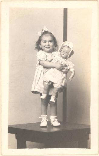 Girl holding doll standing on table, striped background