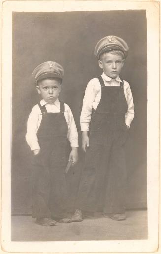 Two standing boys in overalls and navy caps