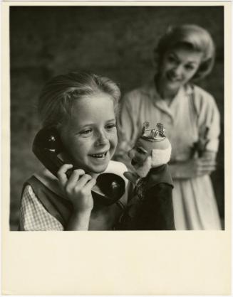 Girl holding telephone and puppet while mother watches