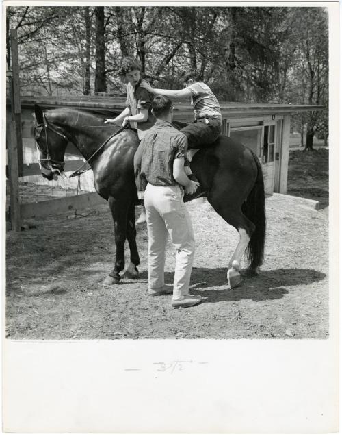 Father helping boy with glasses mount horse, from the series Big Brother