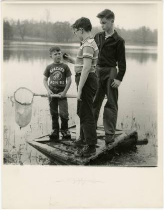 Boy with glasses and two playmates playing on wooden crate in lake, from the series Big Brother